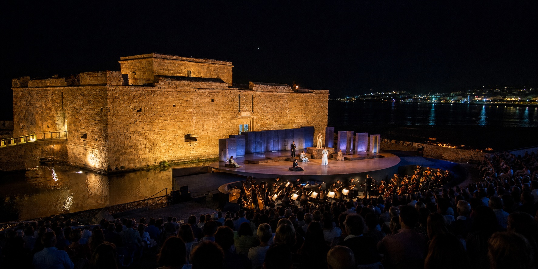 Open-air opera performance beside the illuminated Paphos Castle and Mediterranean harbour at night